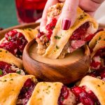 Close up photo of a woman's hand dipping a piece of Thanksgiving Crescent Ring in a small wooden bowl of gravy.