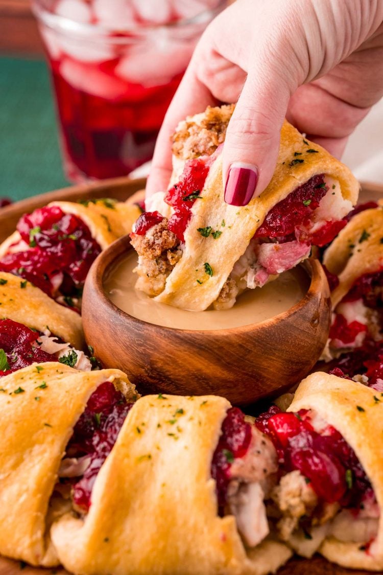 Close up photo of a woman's hand dipping a piece of Thanksgiving Crescent Ring in a small wooden bowl of gravy.