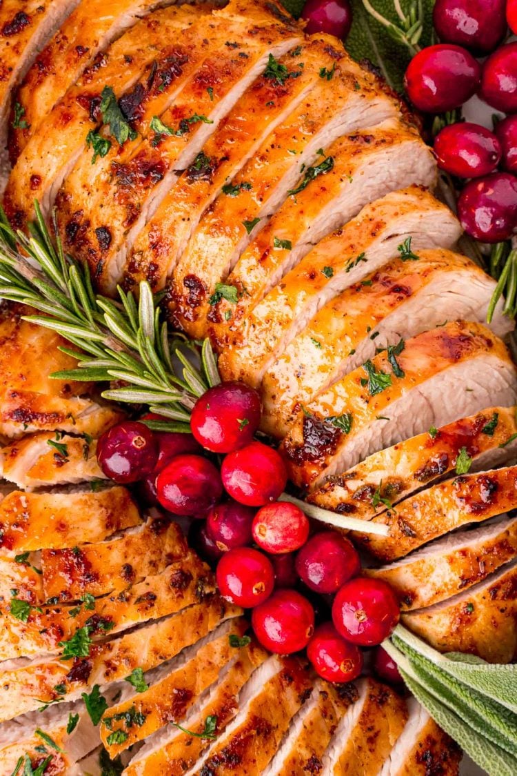 Overhead photo of two sliced turkey tenderloins on a plate with fresh herbs and cranberries for garnish.