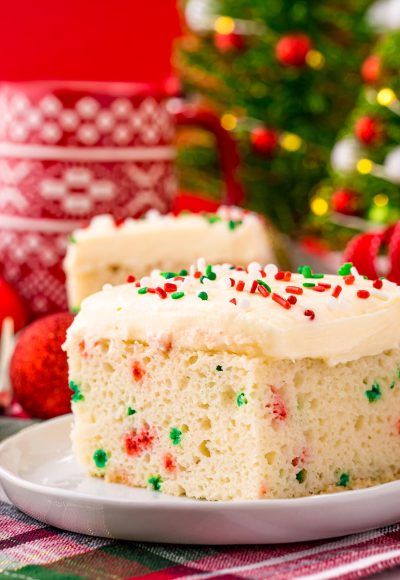 Close up photo of a slice of christmas cake on a white plate with holiday decor in the background.