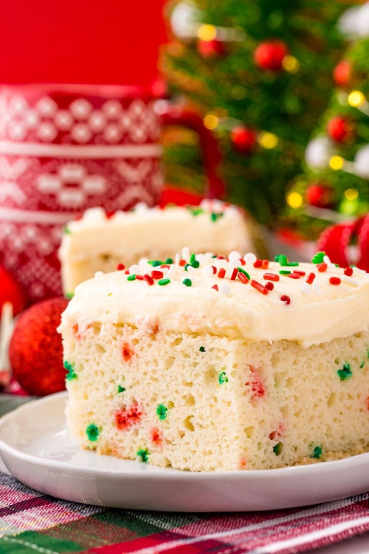 Close up photo of a slice of christmas cake on a white plate with holiday decor in the background.