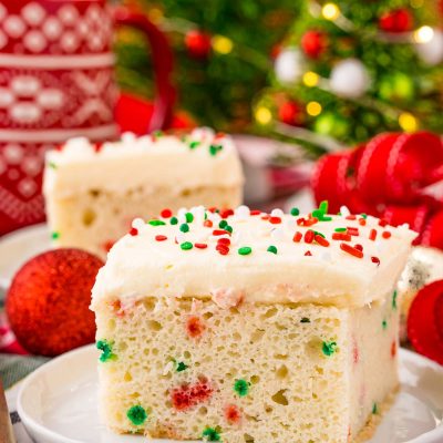 A slice of funfetti Christmas cake on a white plate on a holiday napkin with decor in the background.