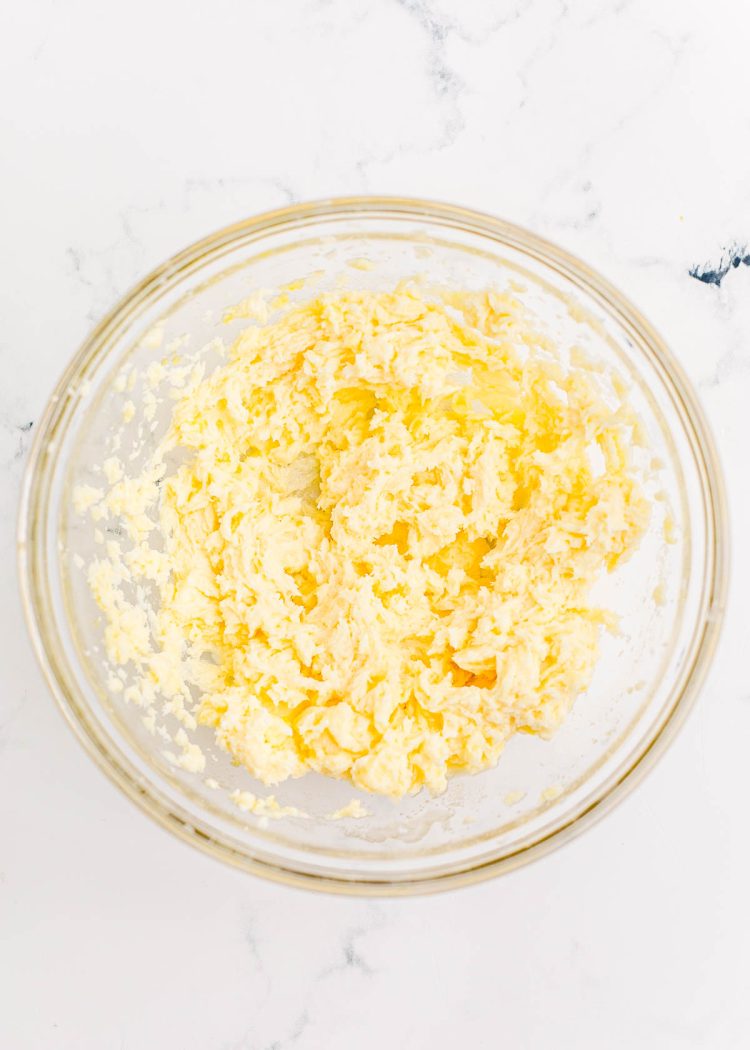 Butter and sugar creamed together in a glass mixing bowl on a marble surface.