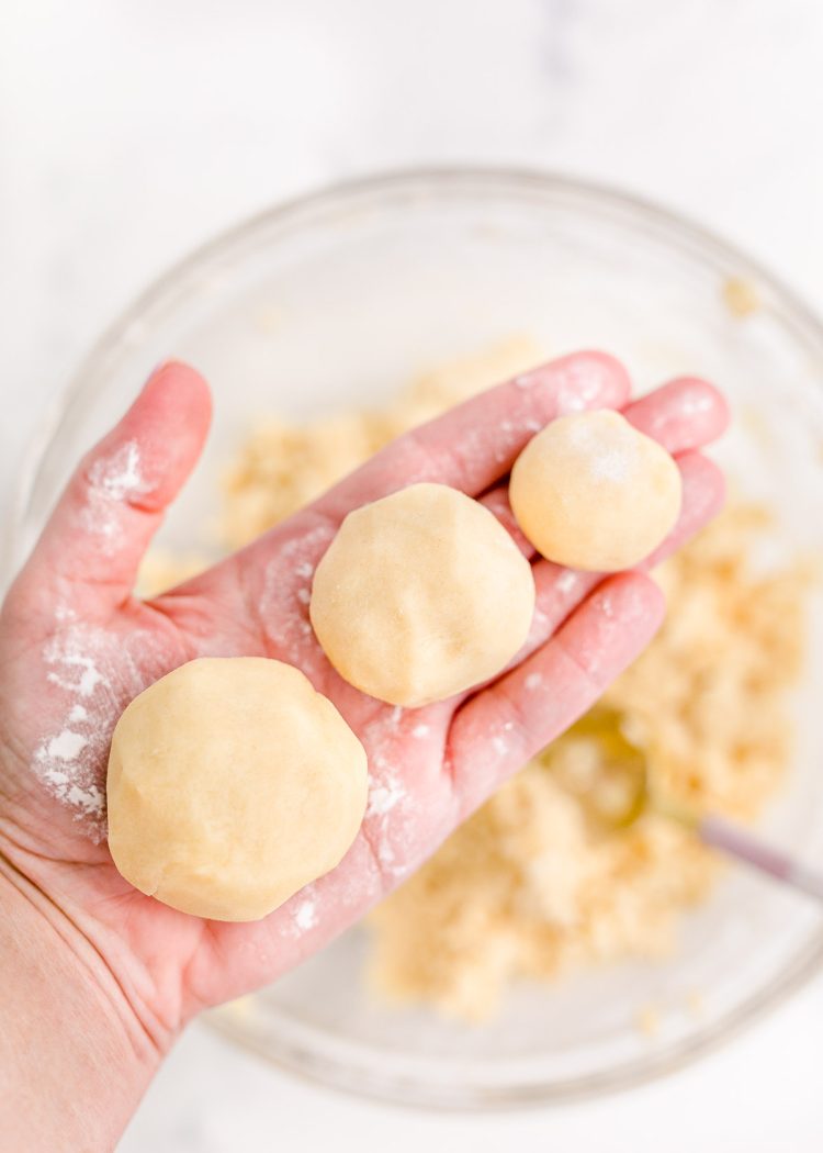 A woman's hand holding three different sized sugar cookie balls.
