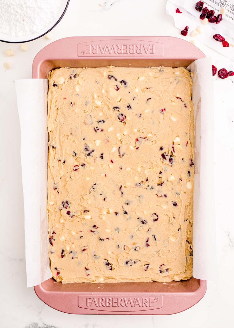 Cranberry bliss bar dough in a pink baking pan lined with parchment paper ready to be baked.