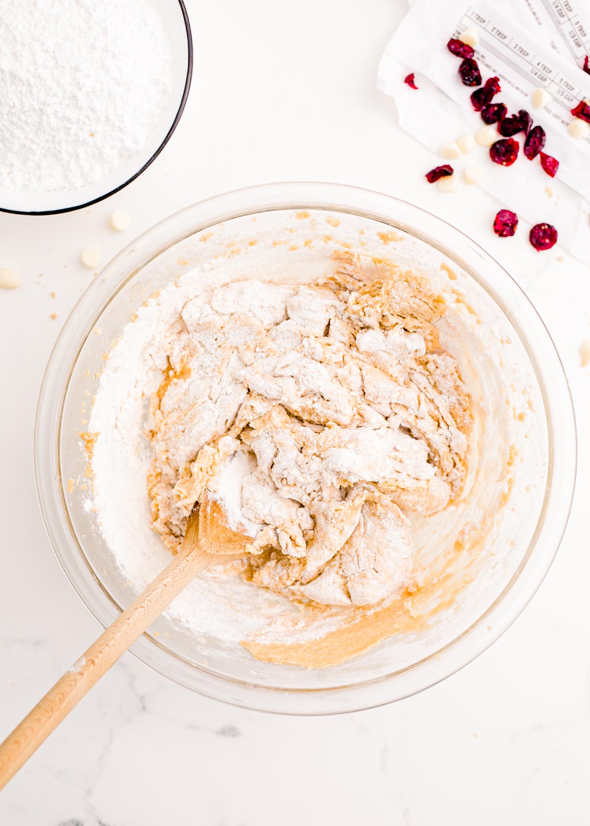 Dry ingredients being mixed with wet ingredients in a large glass mixing bowl to make cranberry bliss bars.