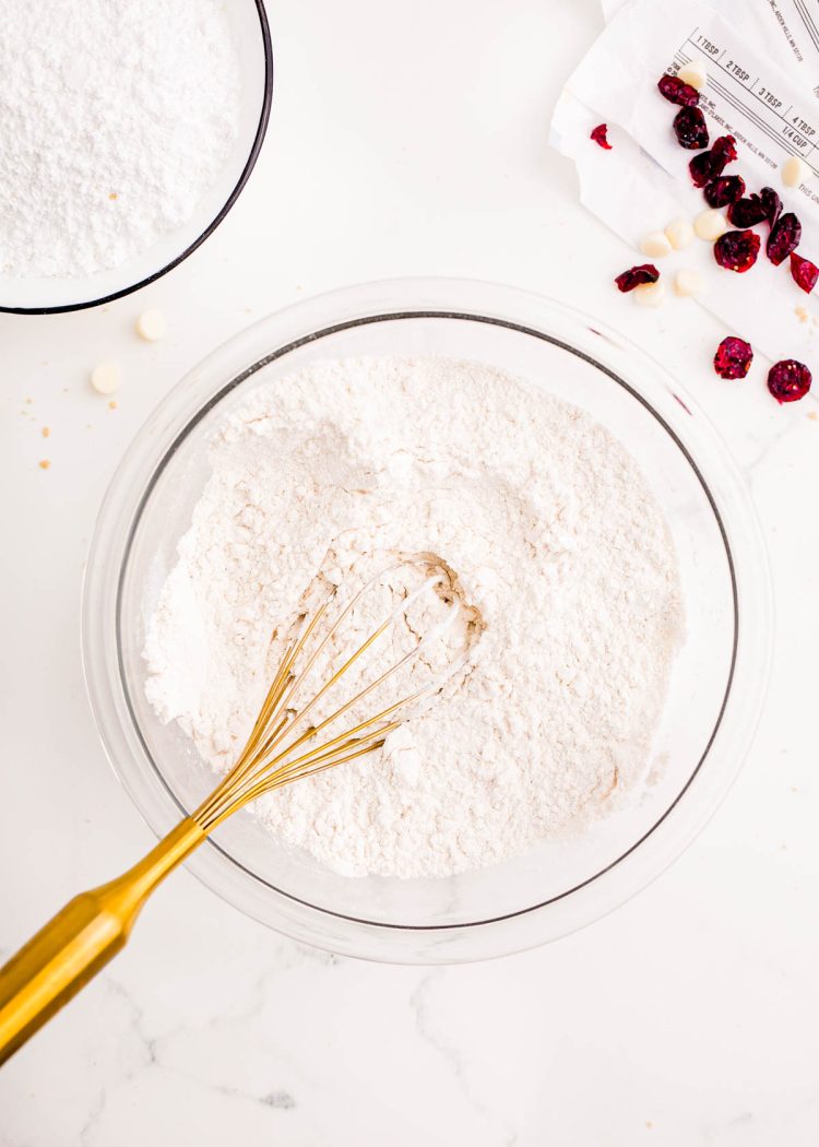 Flour and other baking ingredients being whisked together in a large glass bowl.