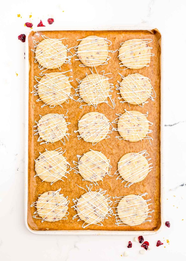 White chocolate drizzled cranberry orange shortbread cookies on a baking sheet.