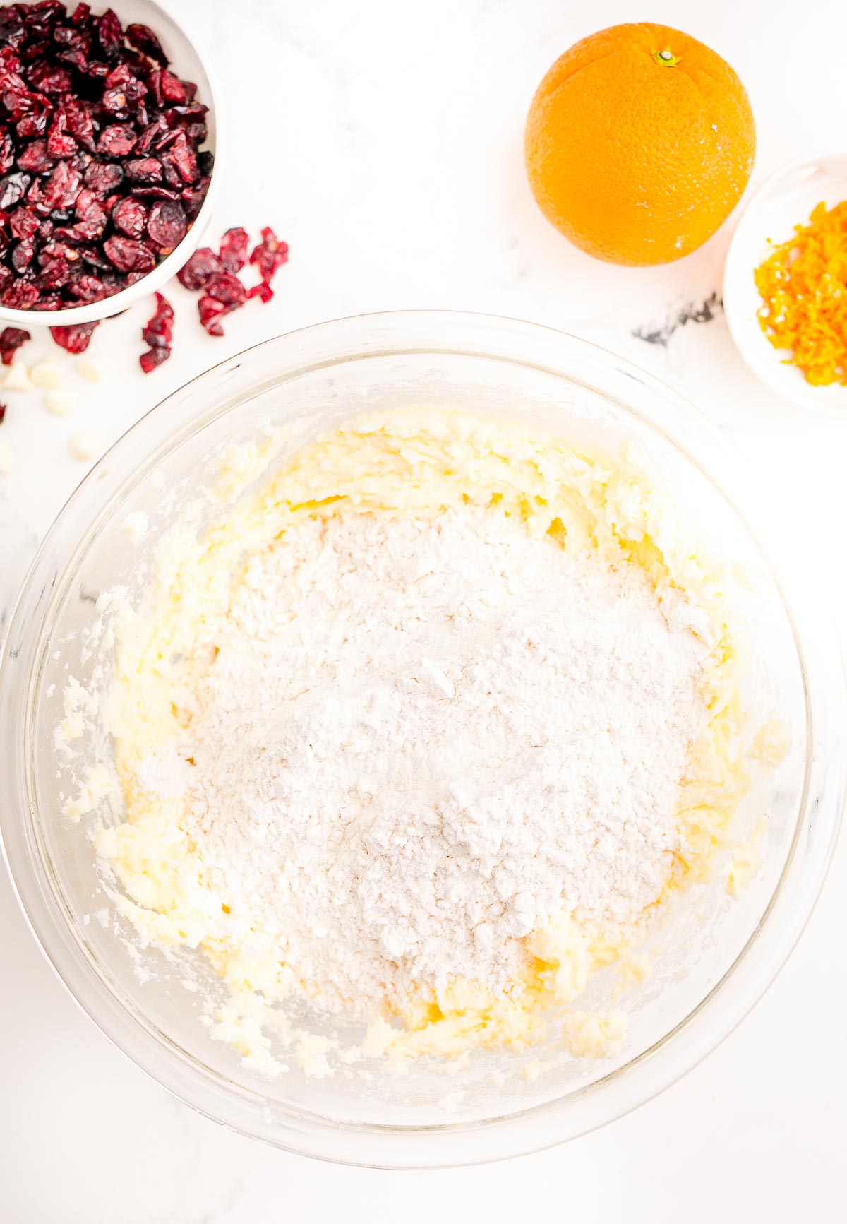 Flour mixture being added to creamed butter and sugar in a large glass mixing bowl.