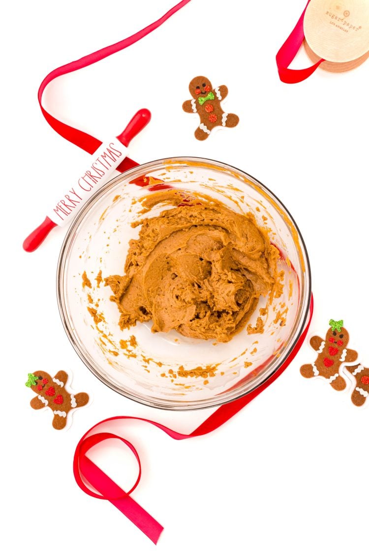 Overhead photo of a glass bowl filled with edible gingerbread cookie dough with red ribbon and gingerbread men around it.