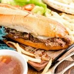 Close up photo of french dip sandwiches on a wooden board with french fries.