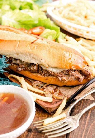 Close up photo of french dip sandwiches on a wooden board with french fries.