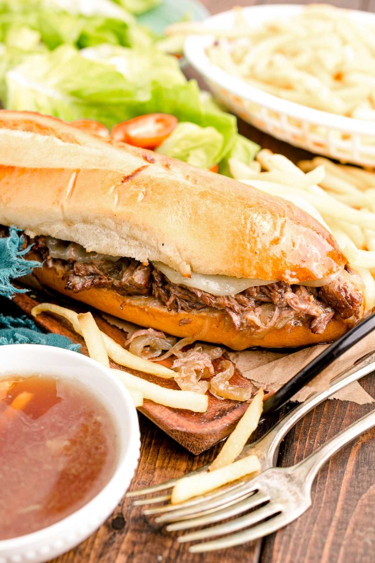 Close up photo of french dip sandwiches on a wooden board with french fries.