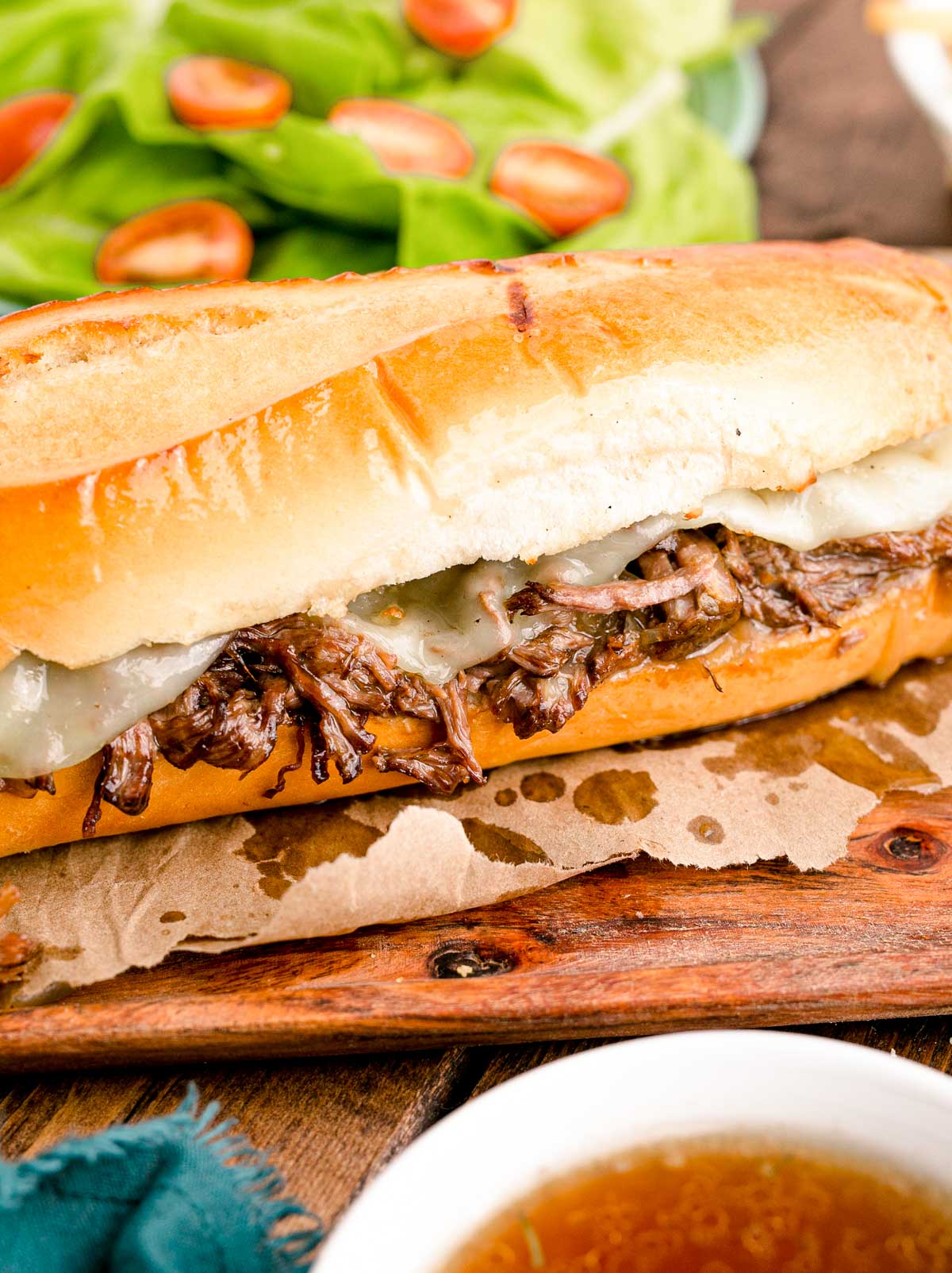 Close up photo of french dip sandwiches on a wooden board with french fries.