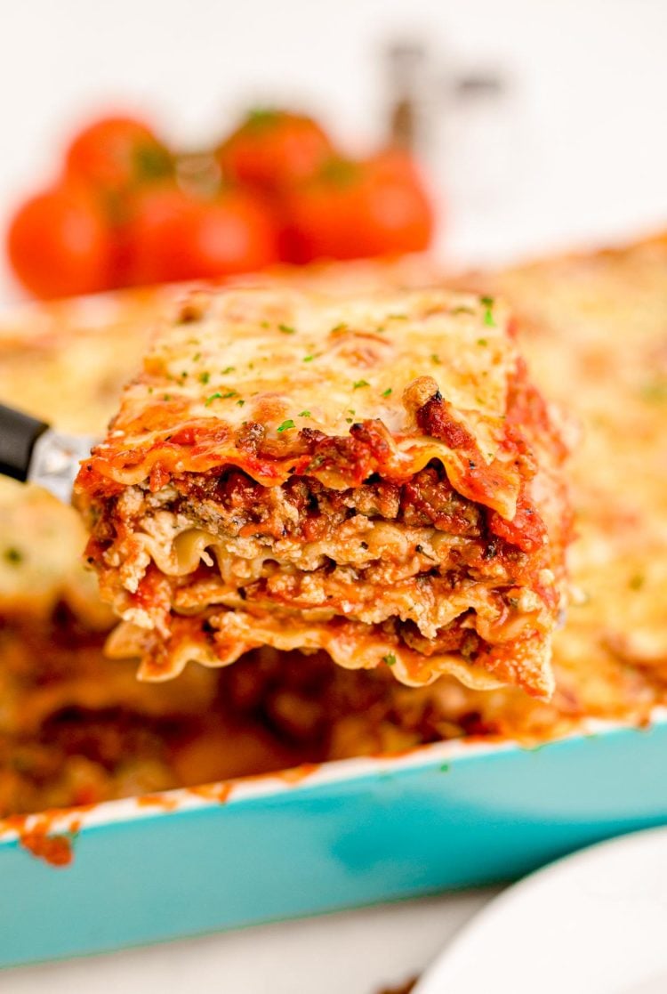 Close up photo of a spatula pulling a slice of lasagna from a teal casserole dish.