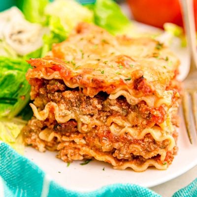 A slice of lasagna on a white plate with a salad.