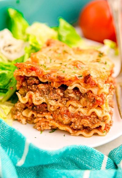 A slice of lasagna on a white plate with a salad.