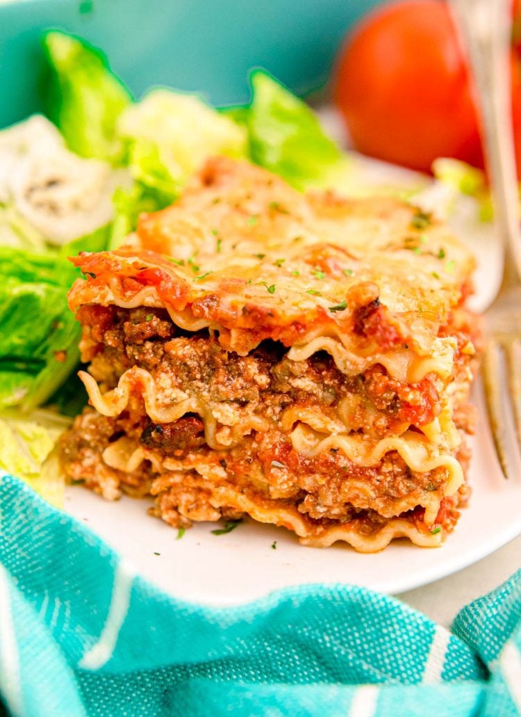 A slice of lasagna on a white plate with a salad.