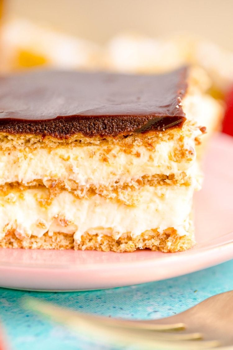 Close up photo of a slice of eclair cake on a pink plate on a blue table.