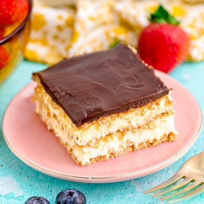 Close up photo of a slice of eclair cake on a pink plate on a blue table.