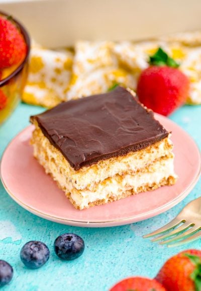 Close up photo of a slice of eclair cake on a pink plate on a blue table.