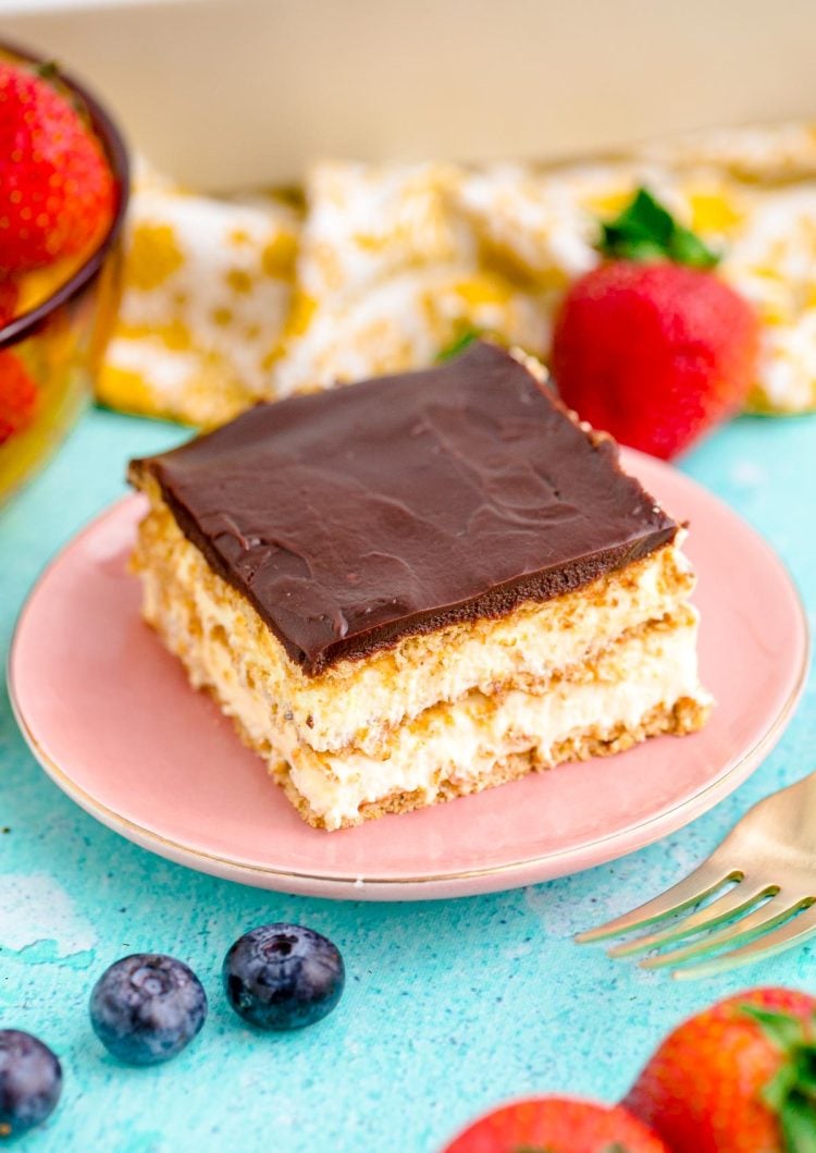 Close up photo of a slice of eclair cake on a pink plate on a blue table.