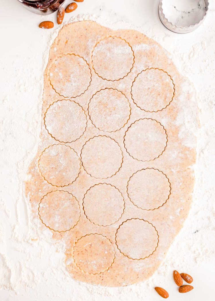 Overhead photo of linzer cookie dough rolled out on a table with round cookies cut out of it.