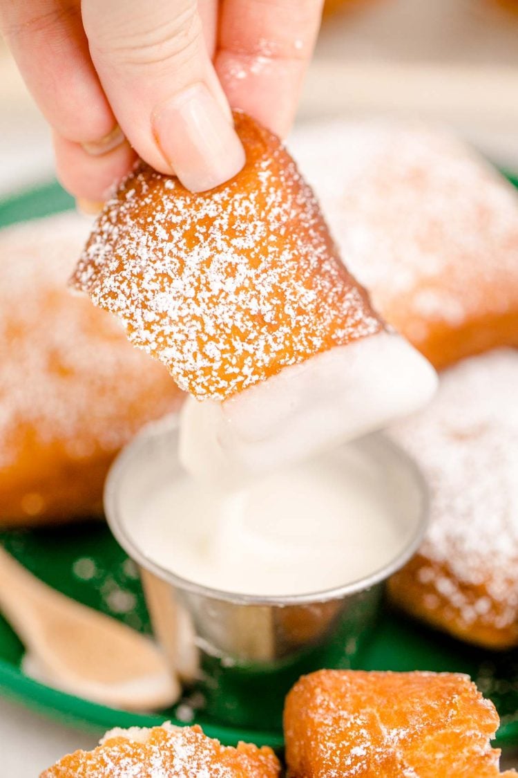 A woman's hand dipping a beignet in icing.