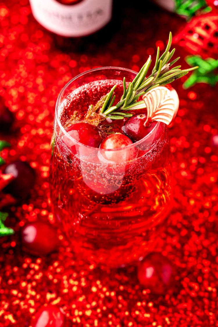 Close up of a poinsettia cocktail in a stemless champagne flute on a red glittery surface.