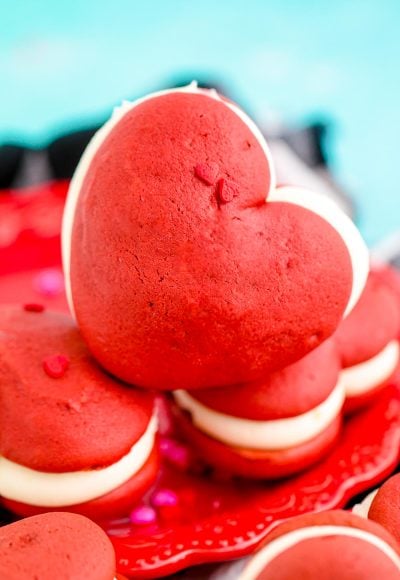 Close up photo of heart shaped red velvet whoopie pies on a red plate.