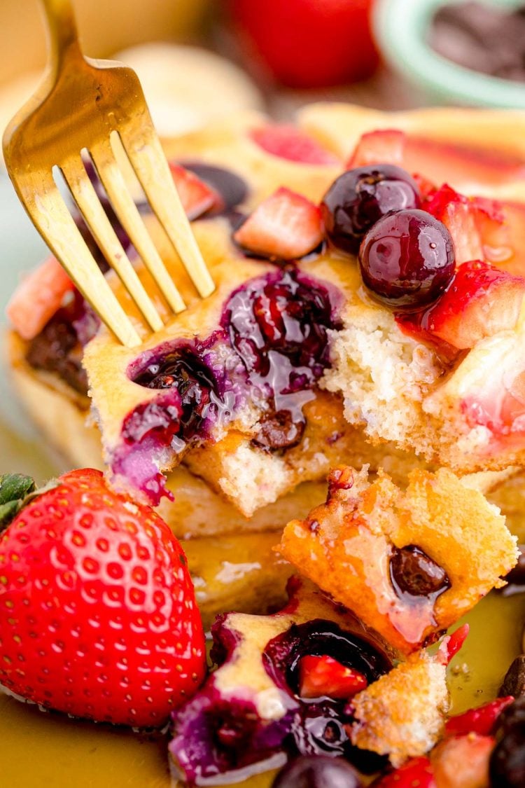 A fork taking a bite out of a stack of sheet pan pancakes with berries.