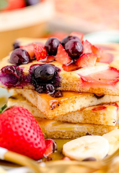 Close up photo of a stack of sheetpan pancakes on a plate with fruit around it.