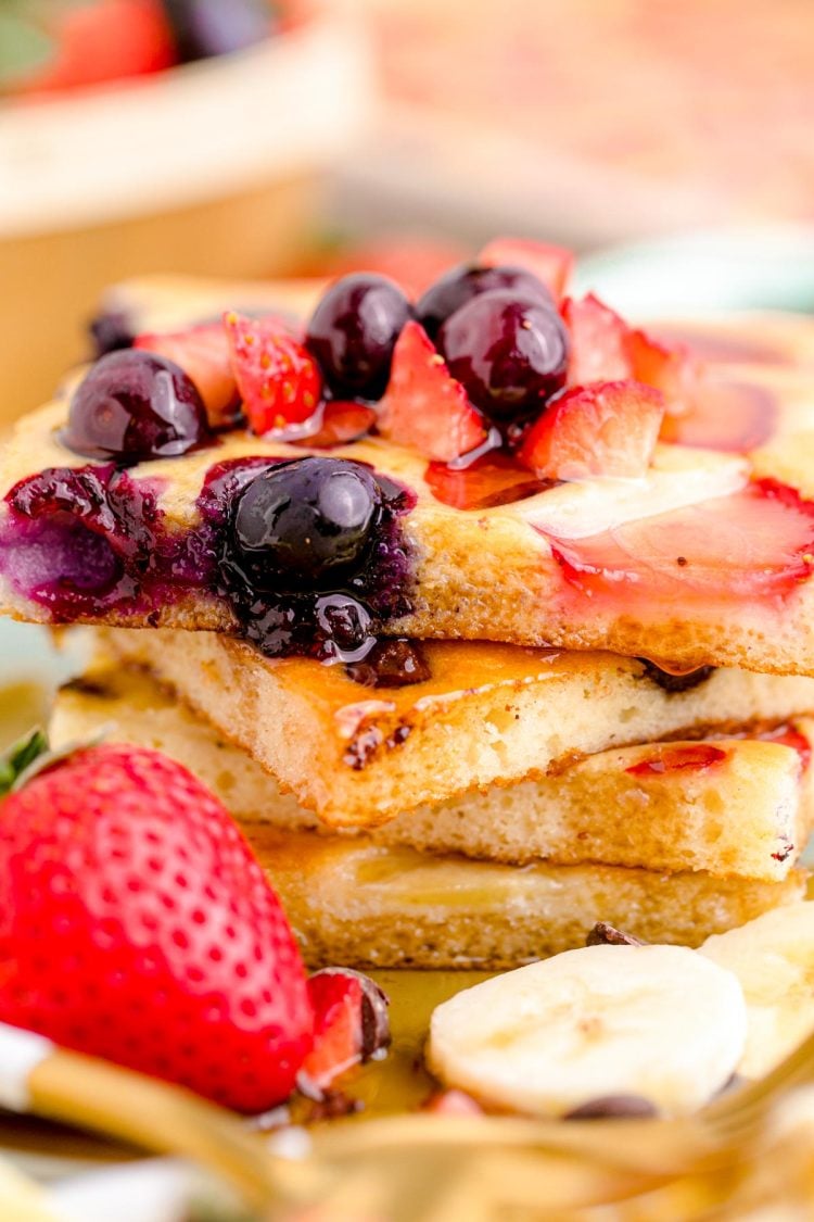 Close up photo of a stack of sheetpan pancakes on a plate with fruit around it.