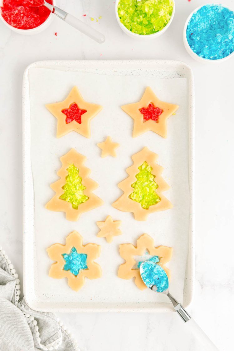 Crushed jolly ranchers being spooned into cut out sugar cookies on a baking sheet. 