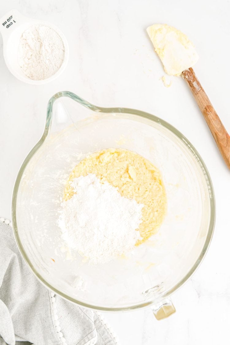 Flour being added to a glass mixing bowl with cookie dough in it.