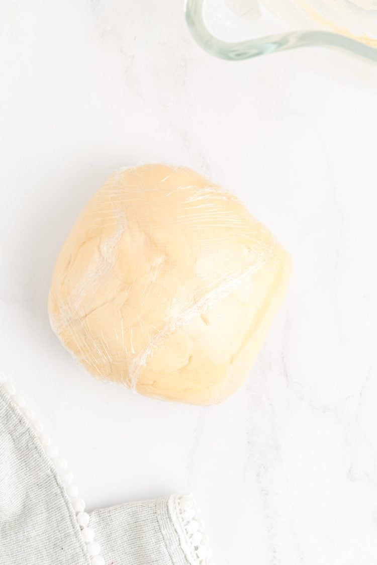 Sugar cookie dough wrapped in plastic wrap on a marble surface.