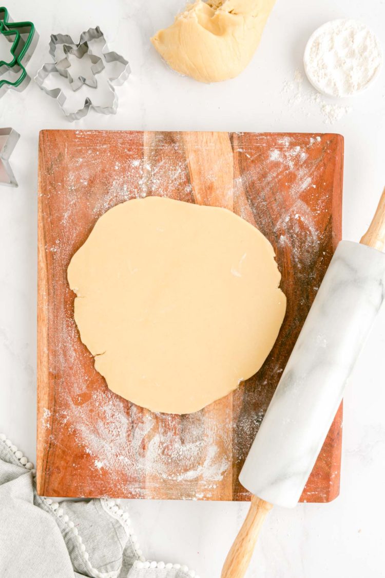 Sugar cookie dough being rolled out on a floured wooden cutting board.