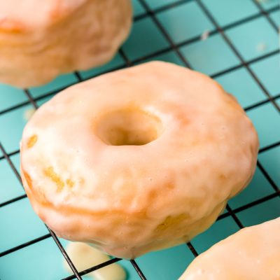 Close up photo of glazed donuts cooling on a wire rack on a teal baking sheet.