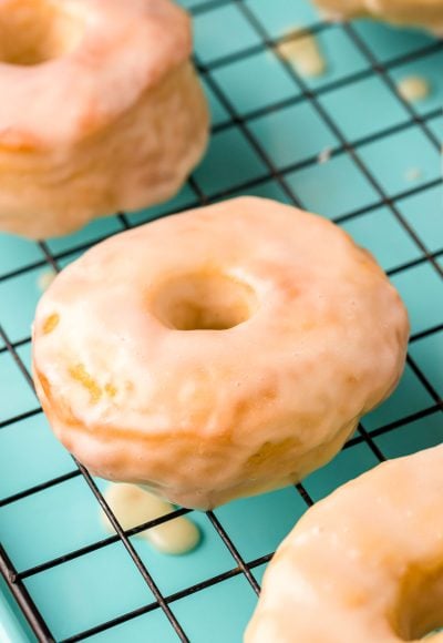 Close up photo of glazed donuts cooling on a wire rack on a teal baking sheet.