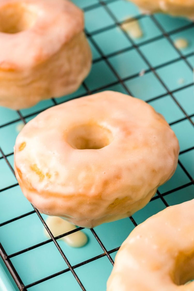 Close up photo of glazed donuts cooling on a wire rack on a teal baking sheet.
