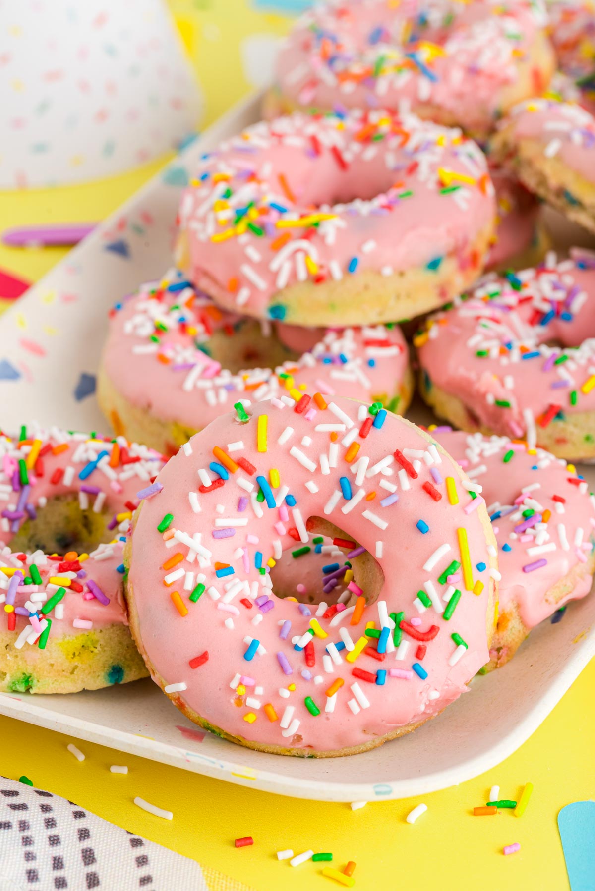 Pink birthday cake donuts on a white serving tray.