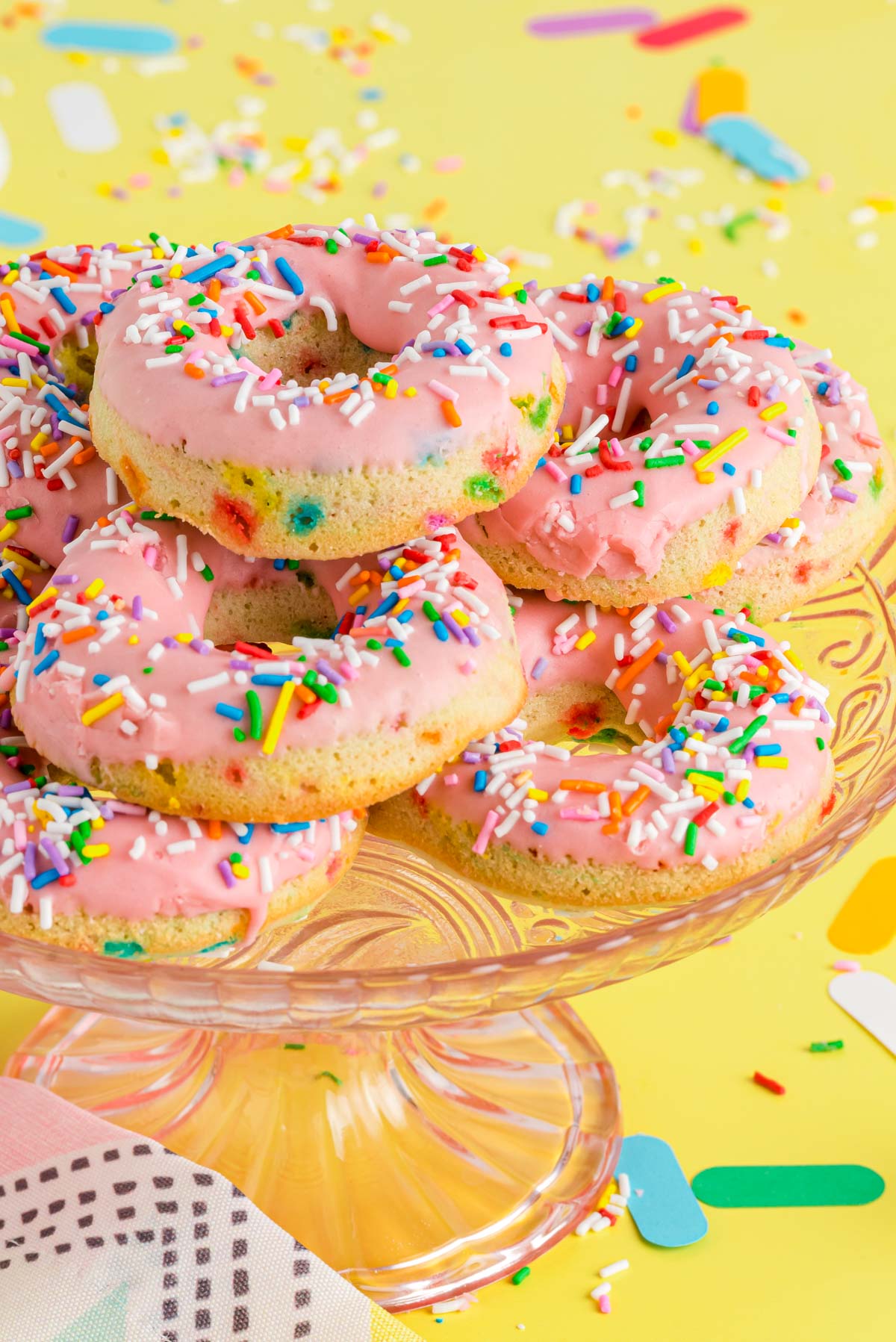 A pink glass cake stand with birthday cake donuts on it.