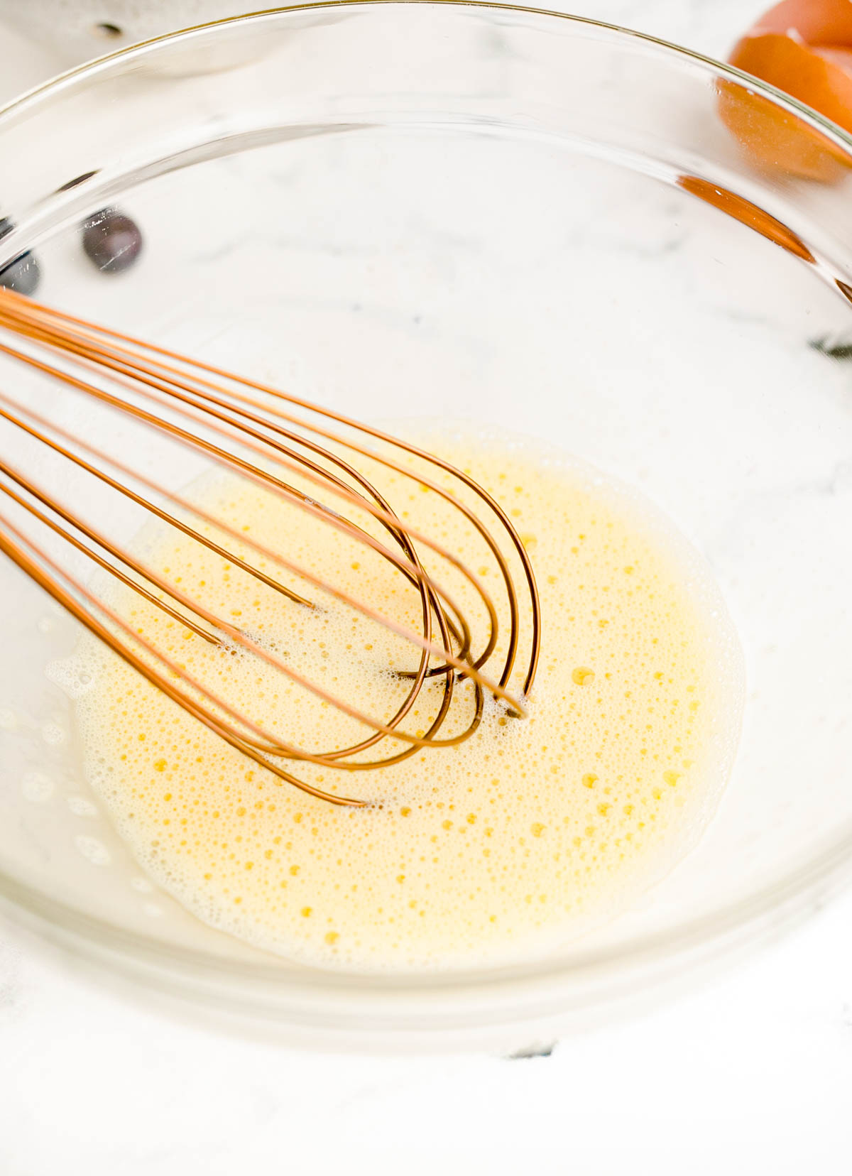 Egg being whisked in a glass mixing bowl.