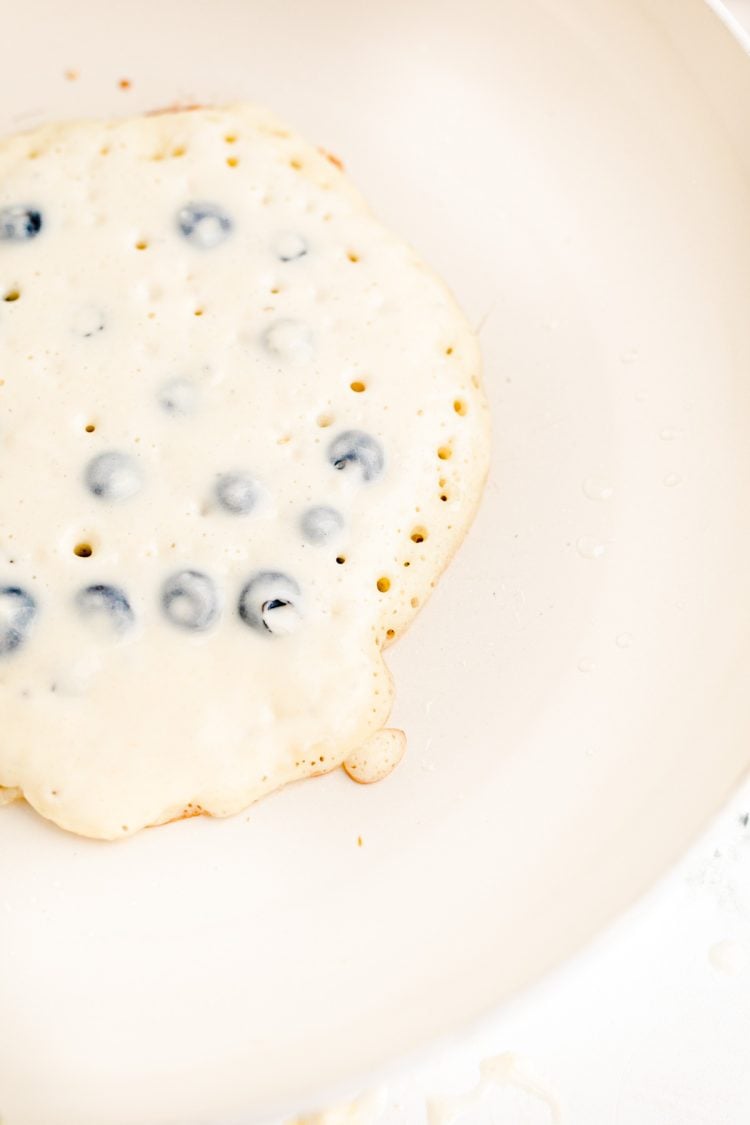 Close up photo of a blueberry pancakes being cooked in a white skillet.