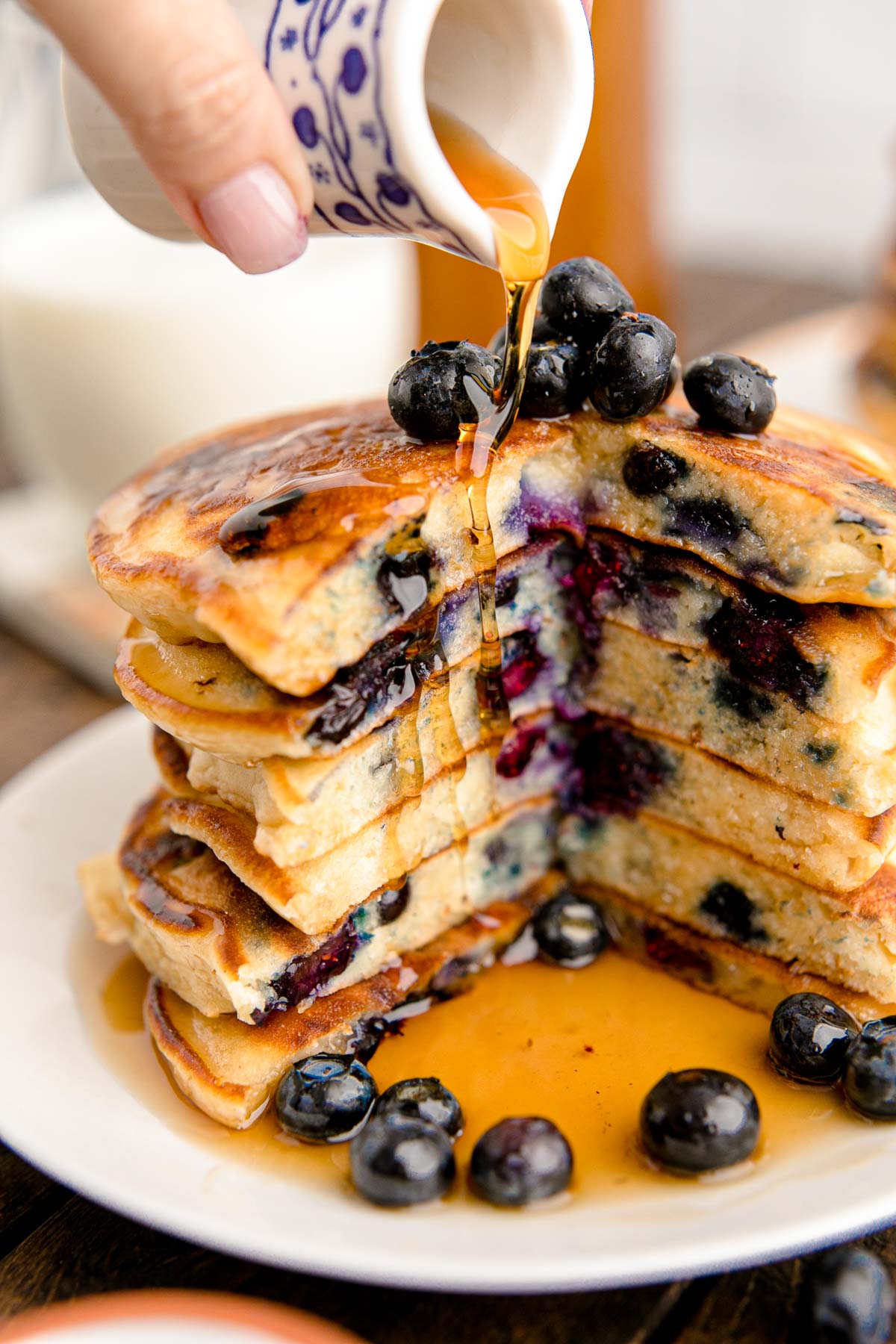A stack of blueberry pancakes with a slice taken out of them getting more maple syrup poured on them.