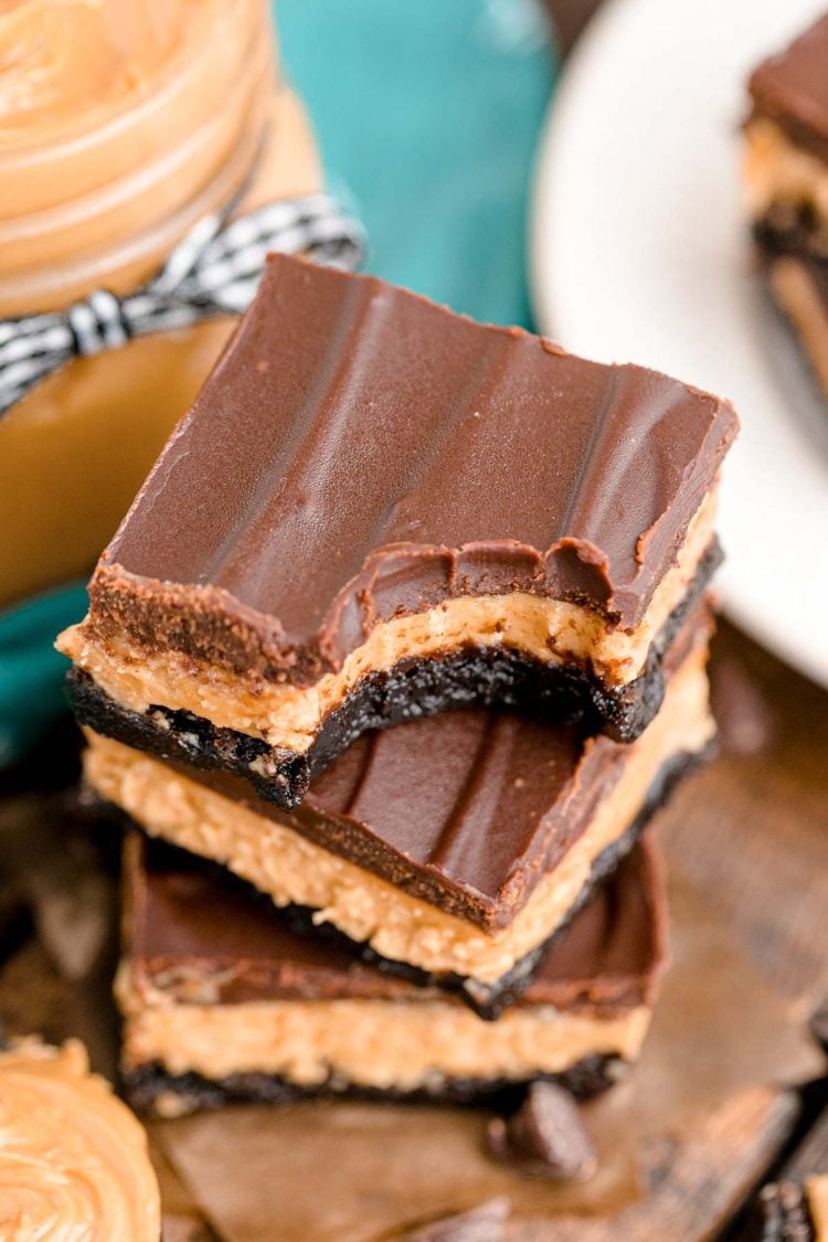 Close up photo of a stack of three buckeye brownies on a wooden table with chocolate chips and peanut butter around it.