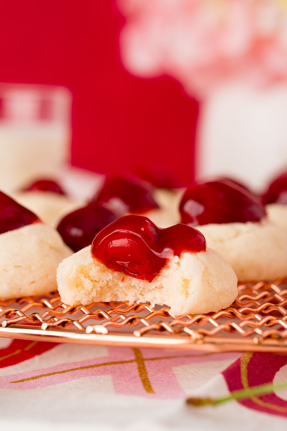 Close up photo of a cherry cheesecake cookie with a bite taken out of it in a copper wire rack.