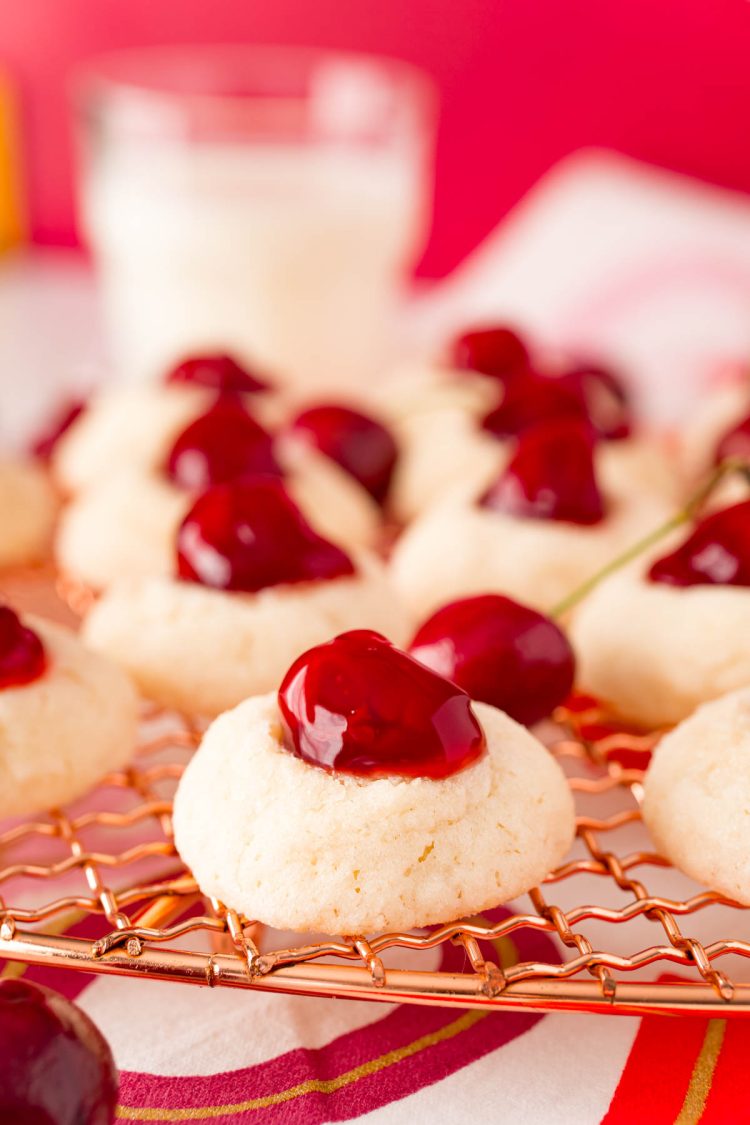 Close up photo of cherry cookies on a copper wire rack with more cookies.
