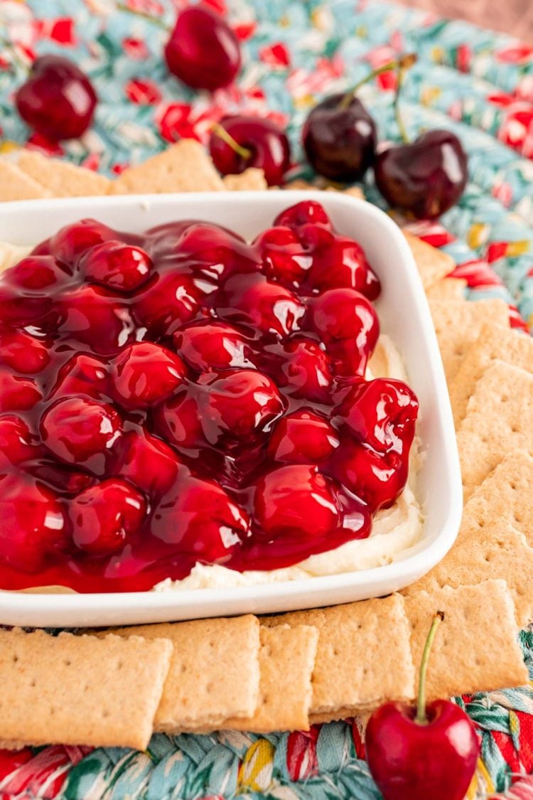 Close up photo of a dish filled with cherry cheesecake dip with graham crackers and fresh cherries around it.