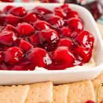 Close up photo of a dish filled with cherry cheesecake dip with graham crackers and fresh cherries around it.